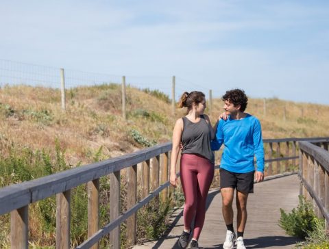 A couple in activewear strolling together on a sunny boardwalk in a natural setting.