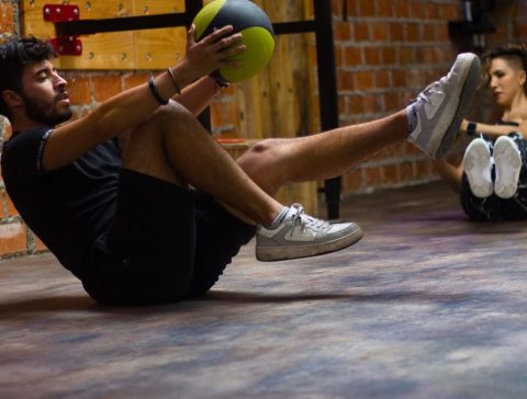A man and woman perform core exercises with a medicine ball in a brick wall gym.